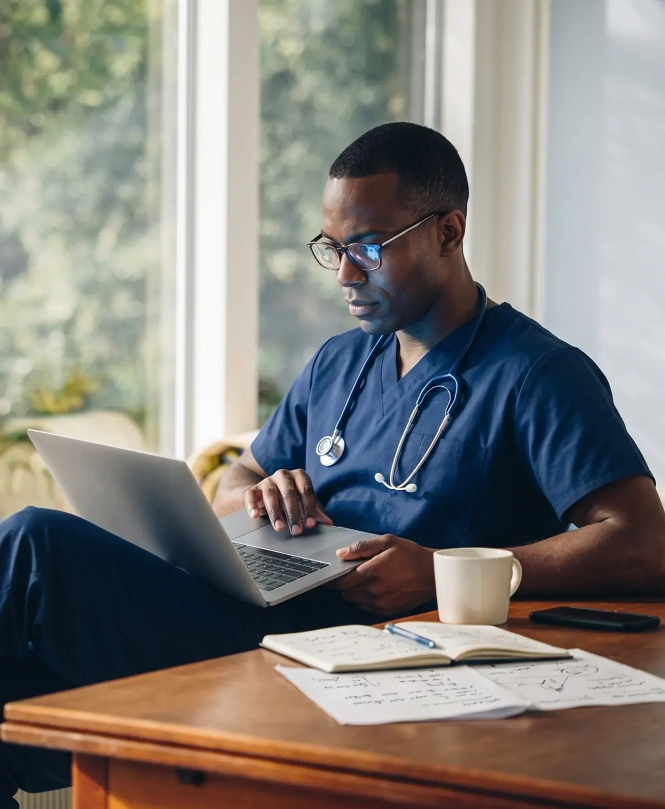 Clinician in scrubs reviewing patient documentation on a laptop