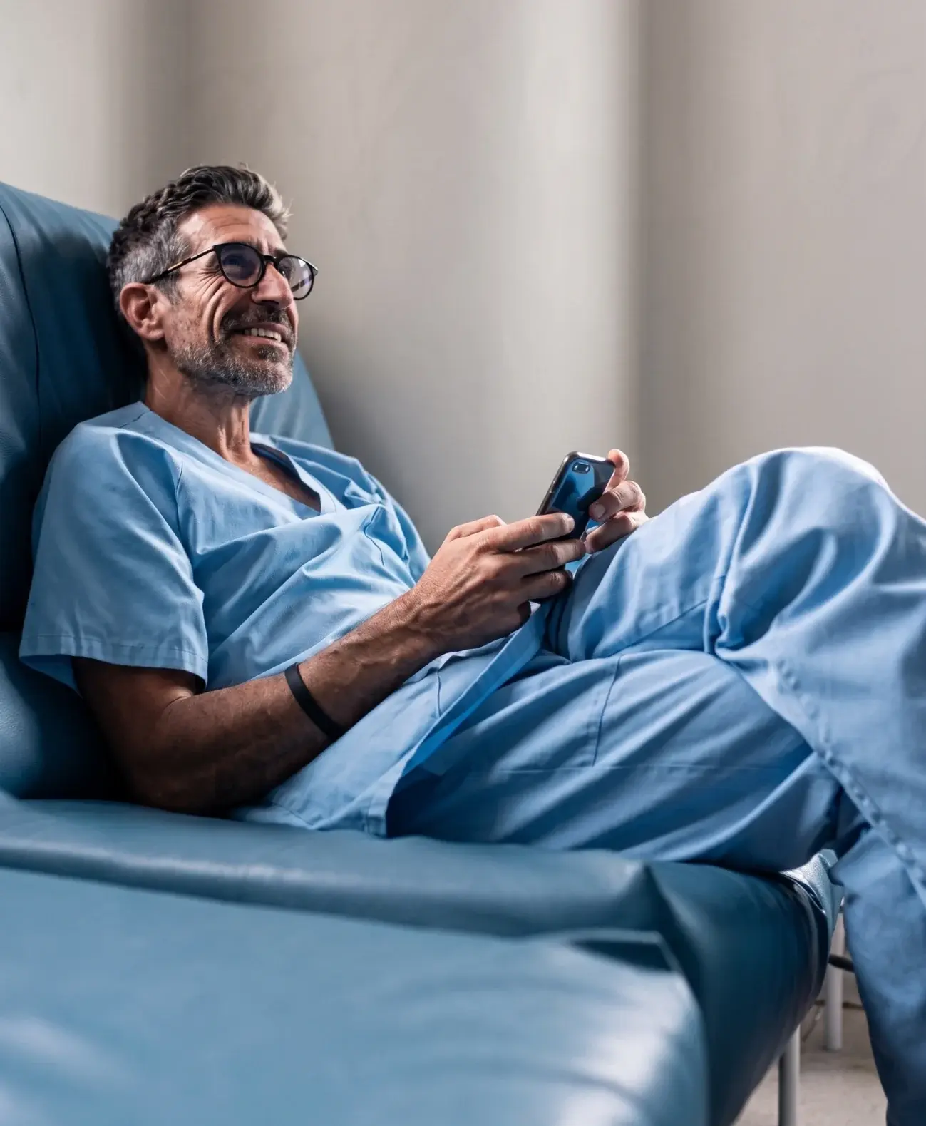 Clinician in scrubs checking a phone while seated in a clinic recliner