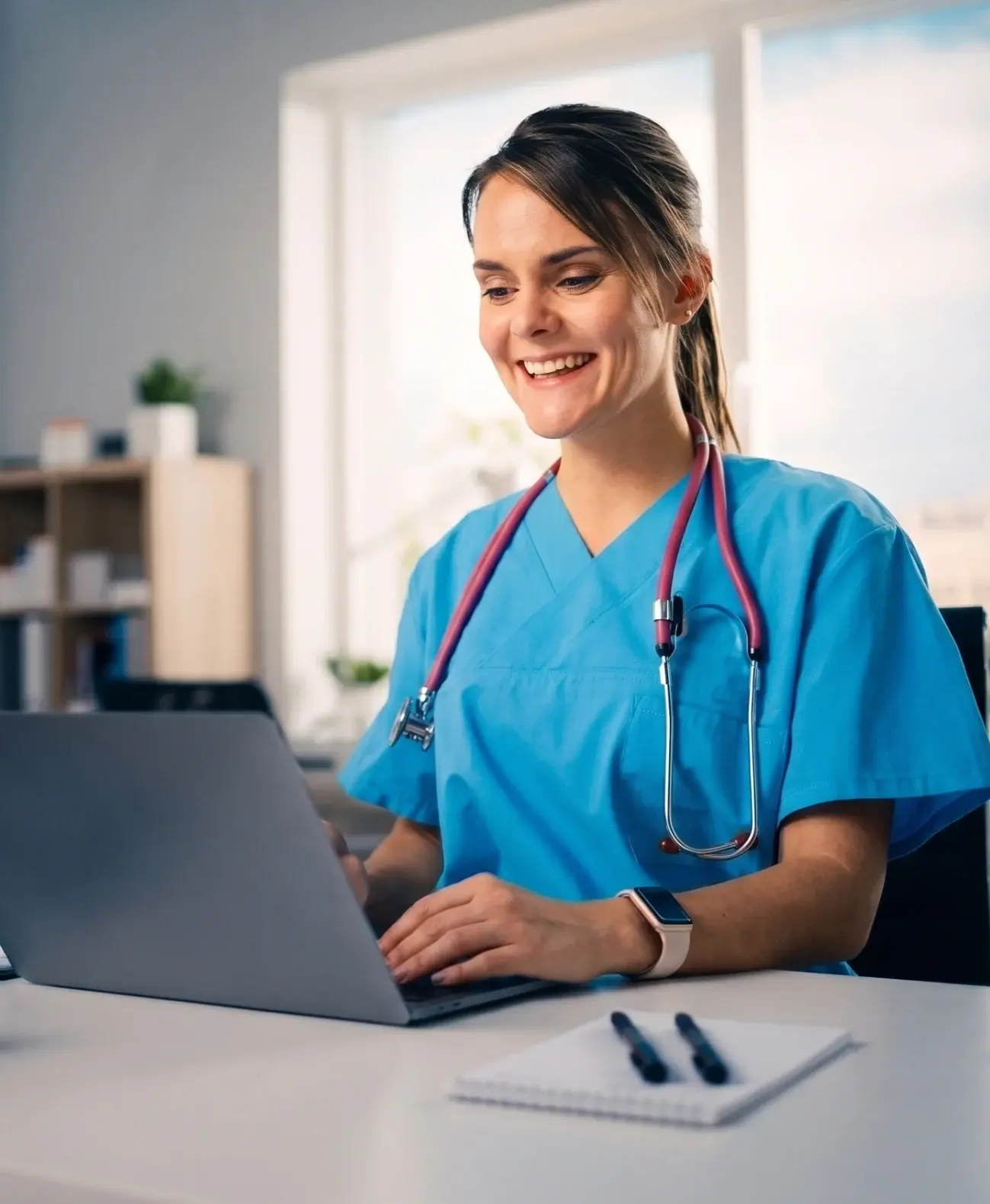 Nurse in scrubs working at a laptop at a clinic desk